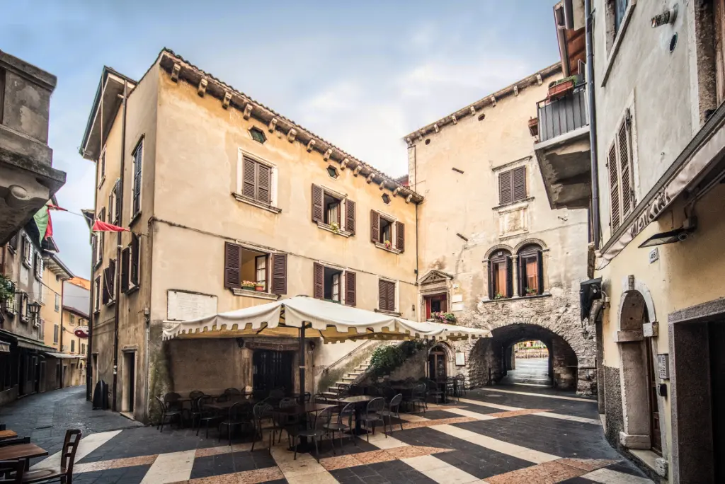 Piazza storica con archi e sedie all'aperto.