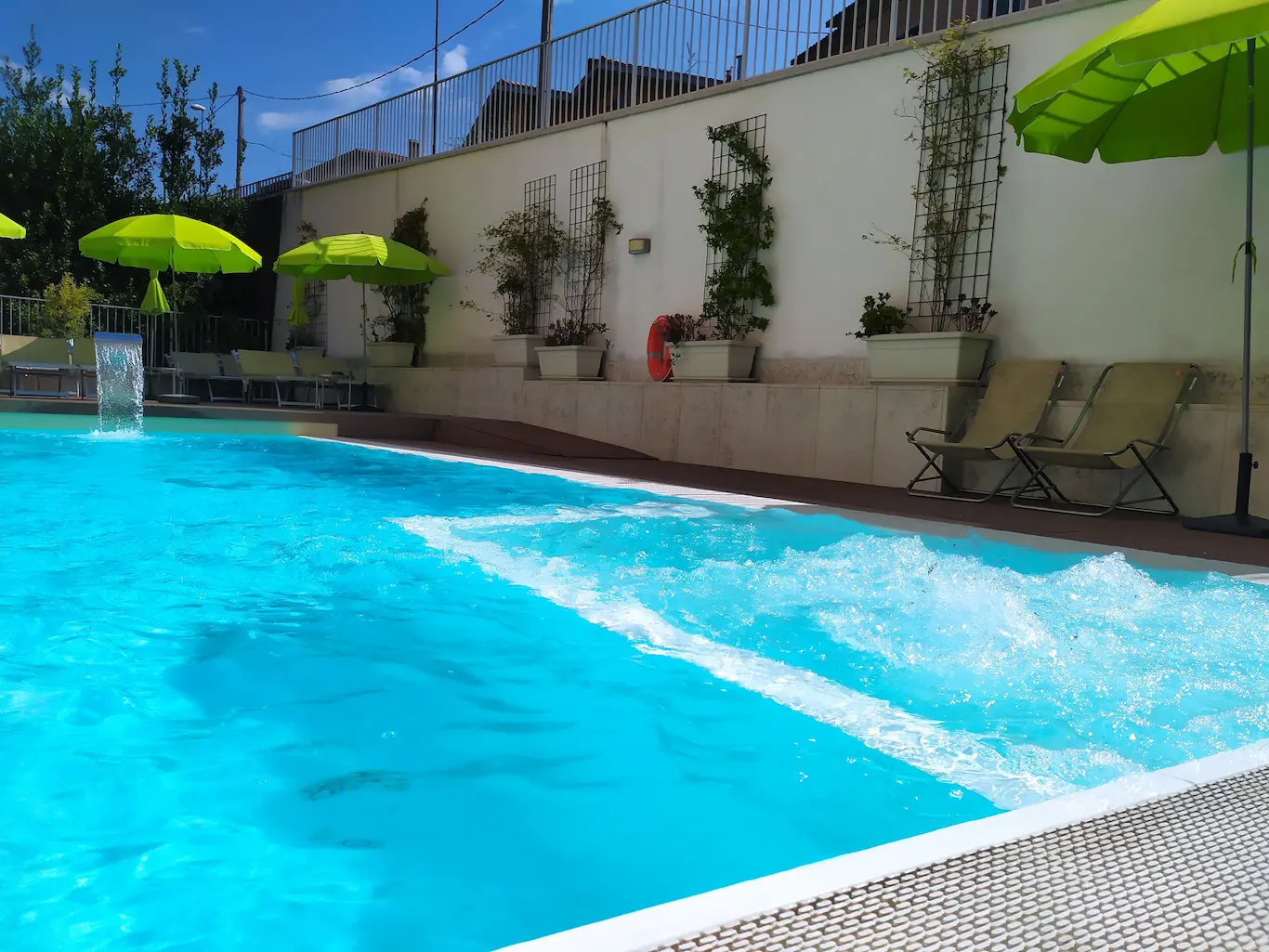 Piscina con ombrelloni verdi e sedie a sdraio.